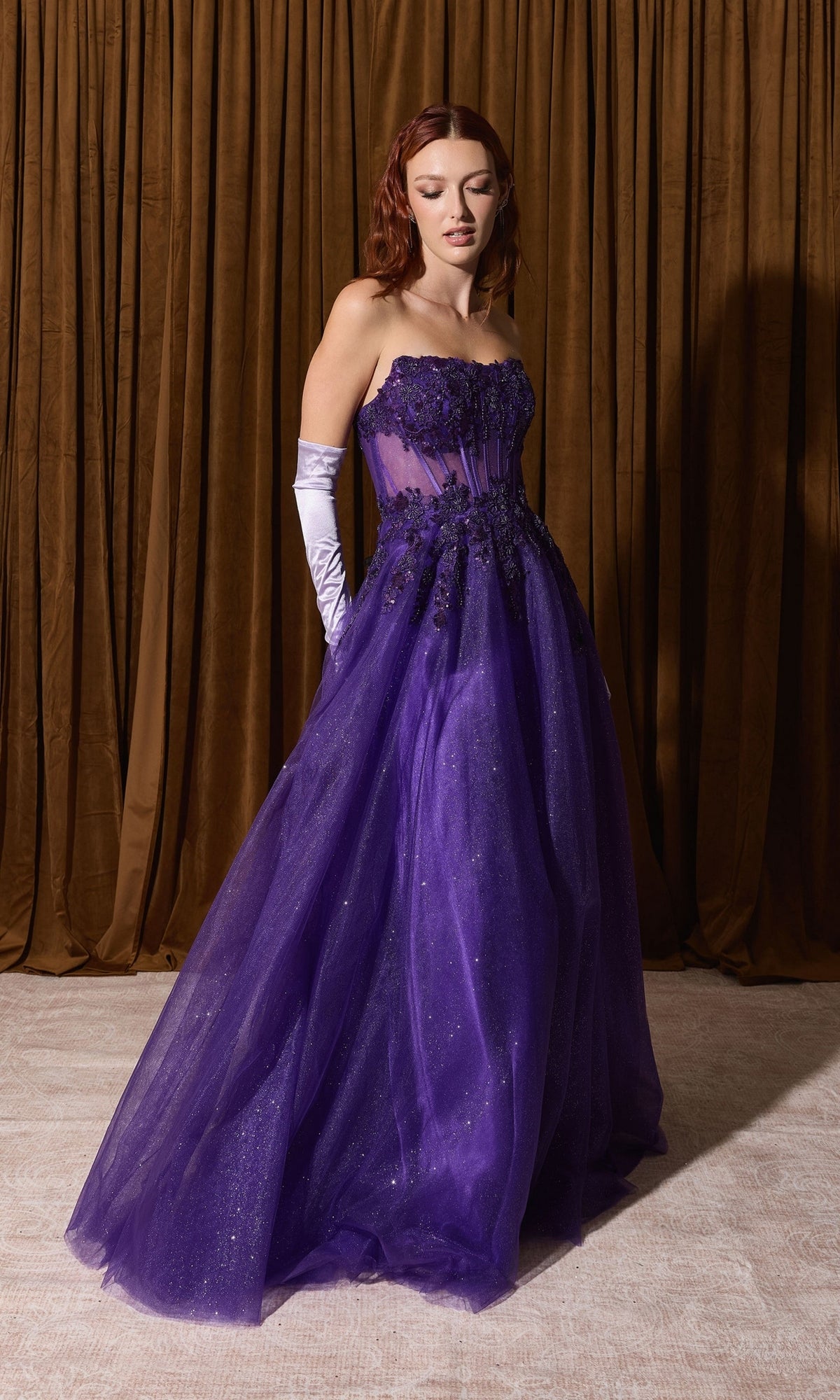 The Eureka EK208 strapless, floor-length purple glitter prom ball gown features a sheer bodice, floral appliqué, and elbow-length gloves.